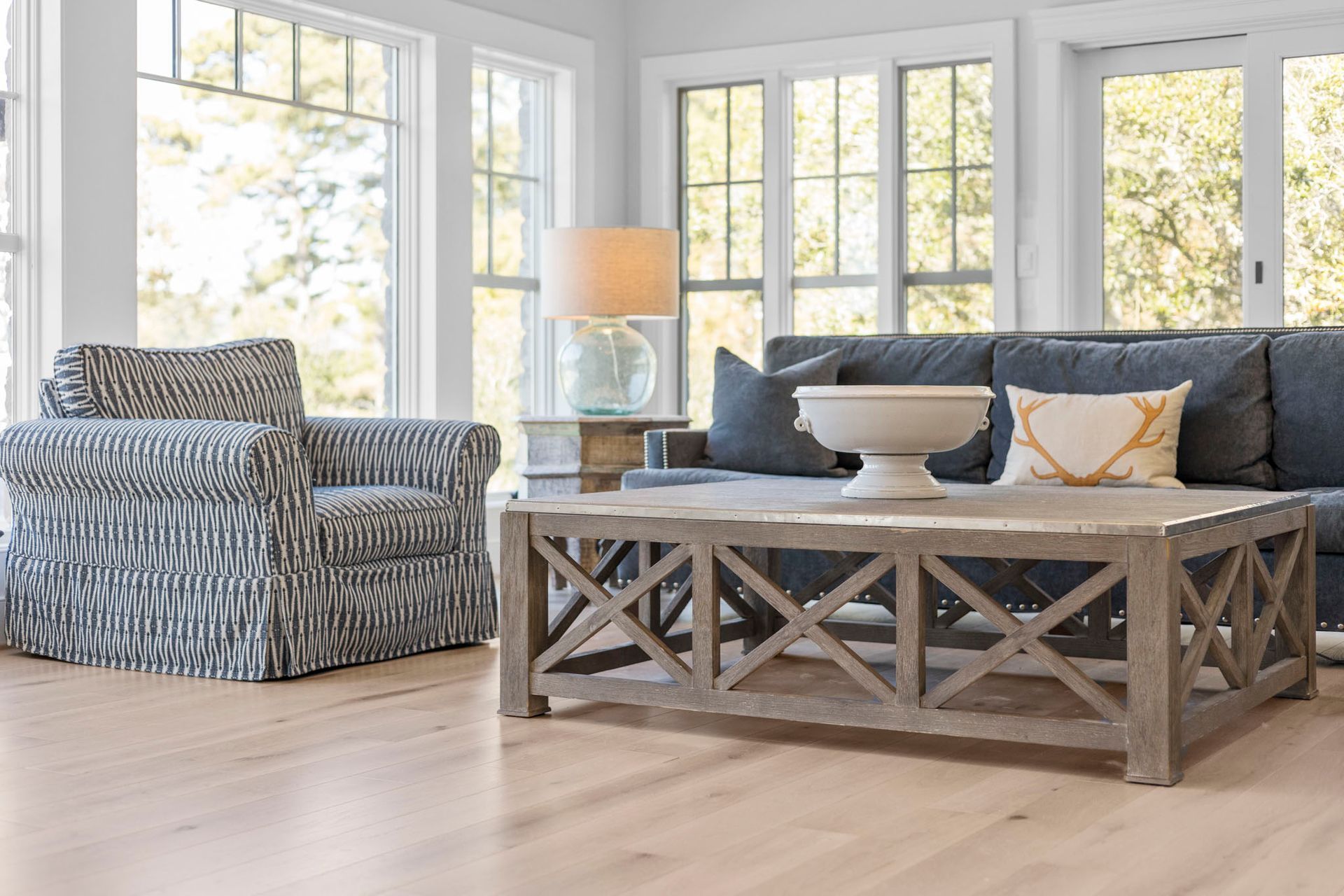 Bright living room with patterned armchair, rustic coffee table, and large windows.