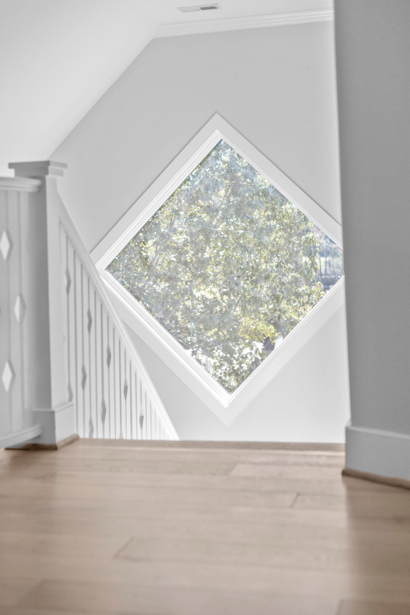 Bright foyer with a diamond-shaped window and light wood floor, showing trees outside