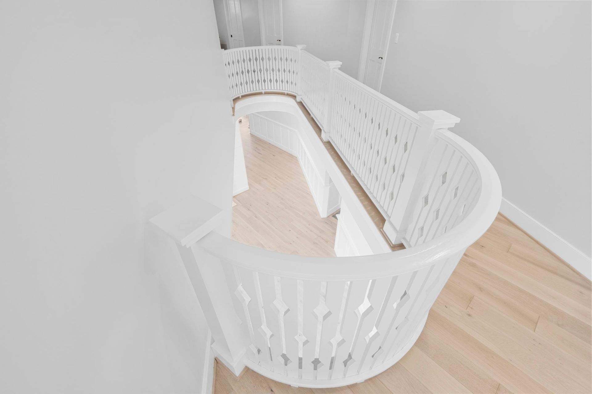 White curved staircase with ornate railing and light wood steps in a bright interior
