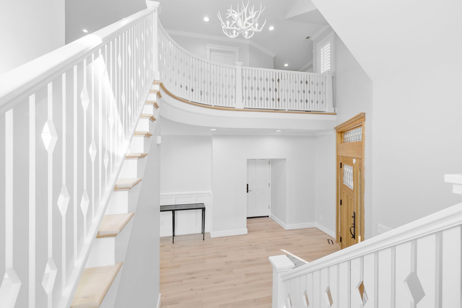 Bright white foyer with staircase, chandelier, wood floors, and a gold front door