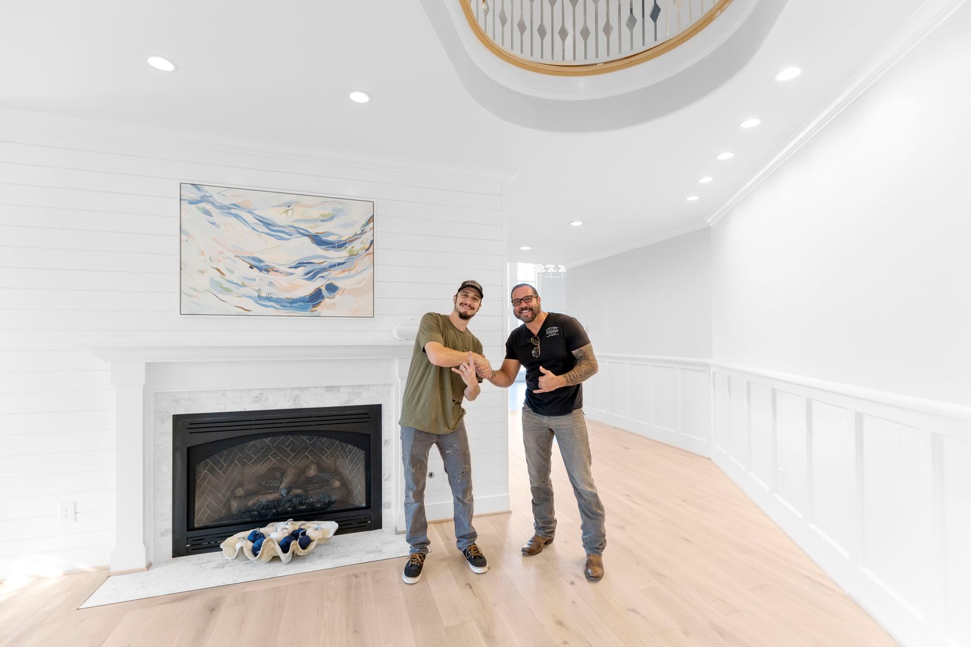 Two people in a bright white living room, holding a baby near a fireplace and abstract wall art.