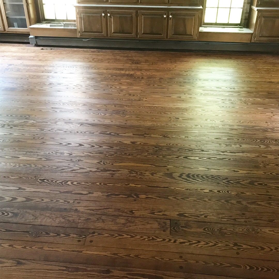 Wooden floor in a sunlit room with windows and a cabinet along the back wall