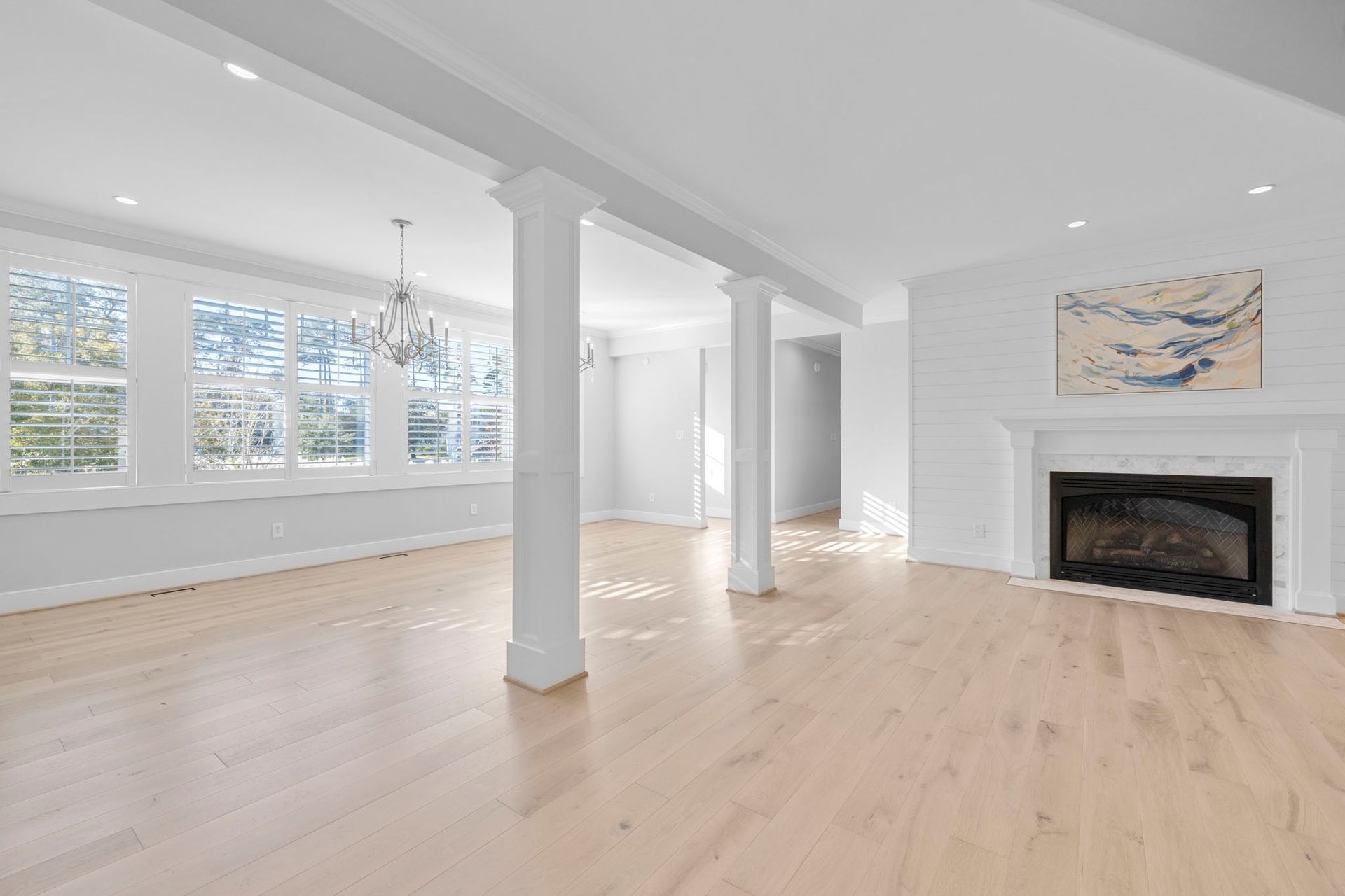 Bright open living room with white columns, light wood floors, large windows, and a fireplace
