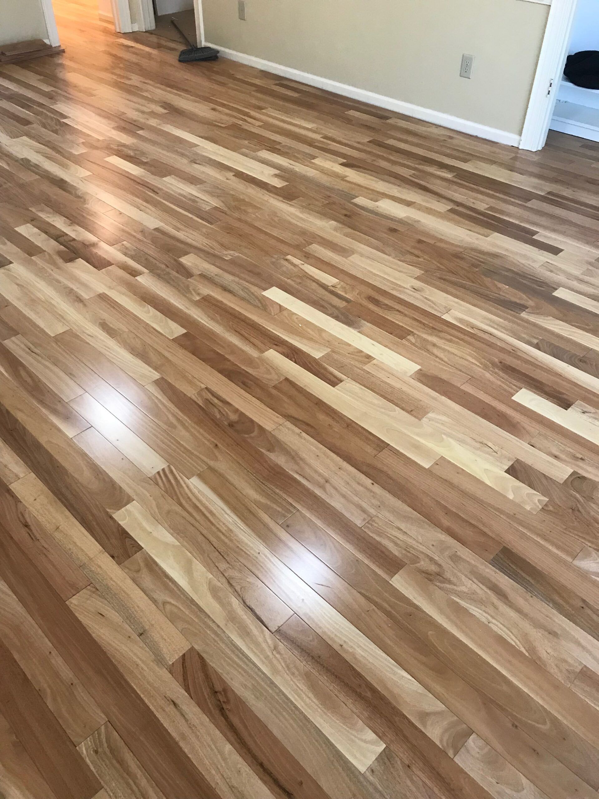 Empty room with glossy wood-look floors and beige walls, lit by sunlight.