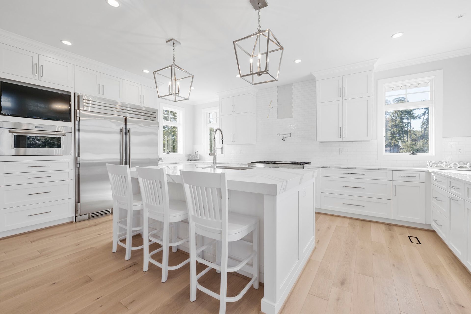 Bright white modern kitchen with island, bar stools, stainless steel appliances, and wood floors