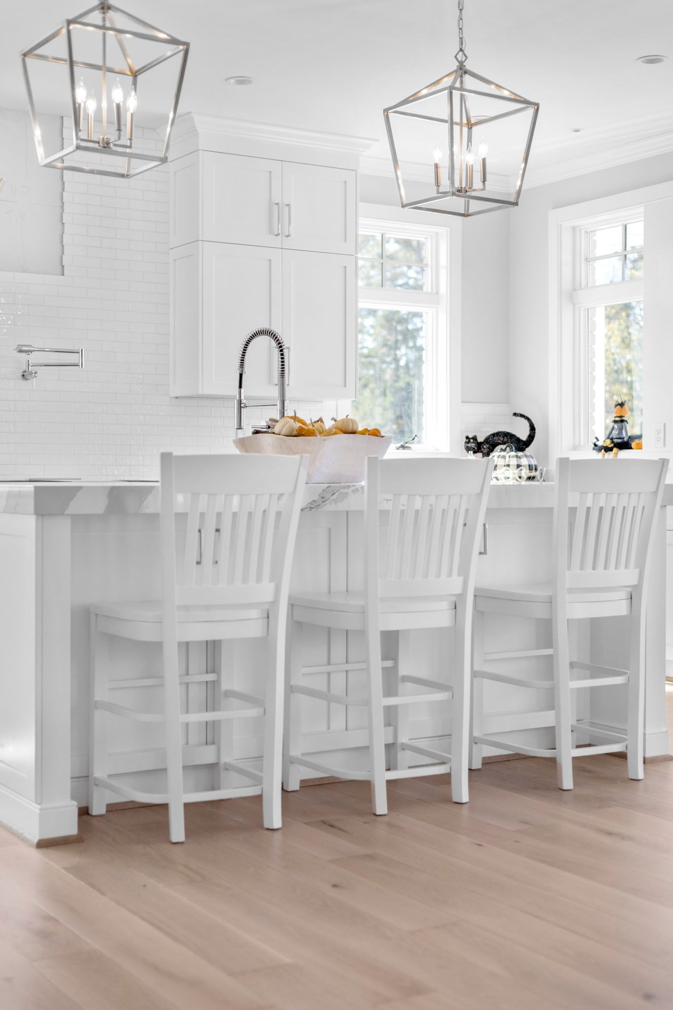 Bright white kitchen with island, bar stools, pendant lights, and light wood floors