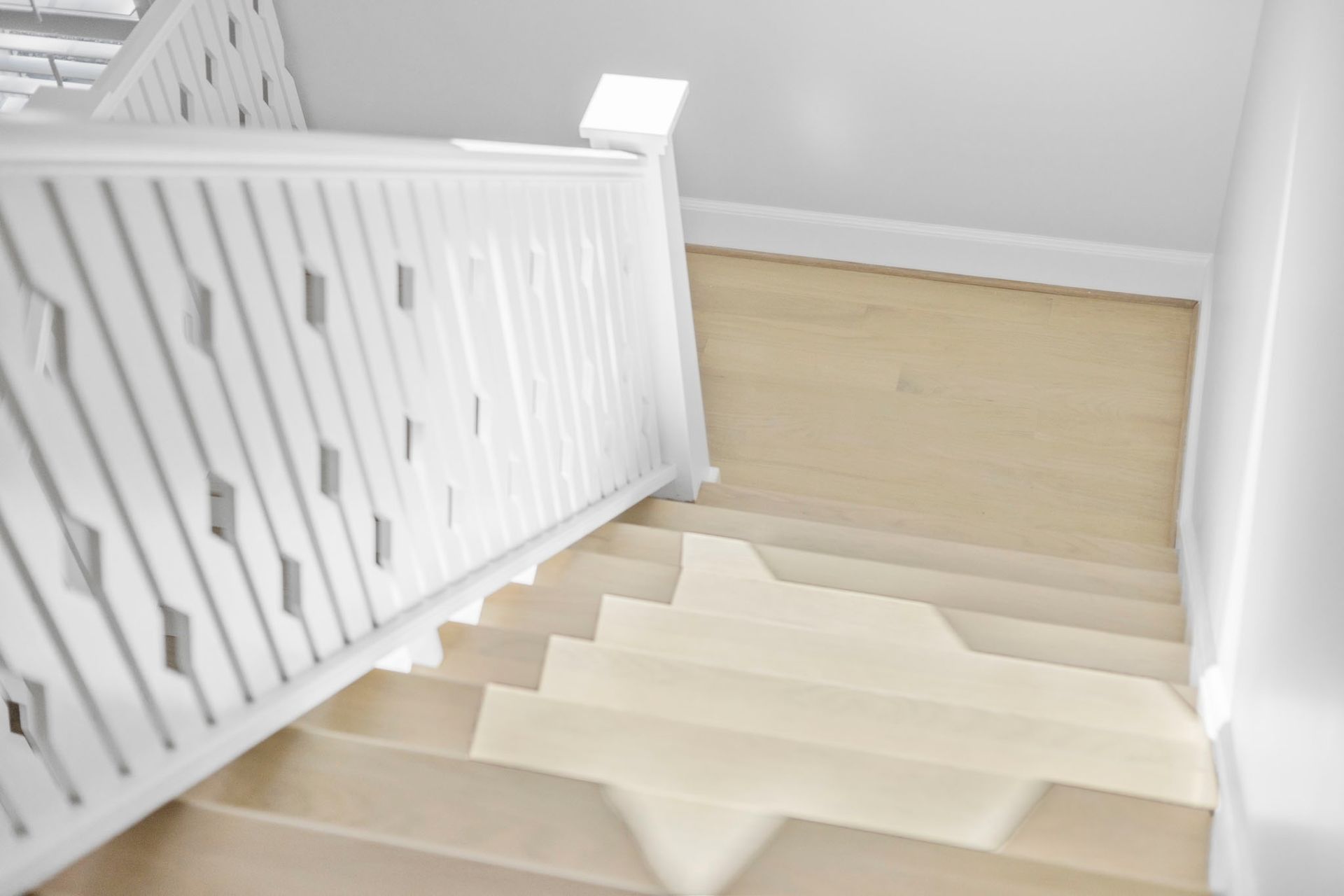 Bright staircase with white railing and light wood steps leading to a hallway.