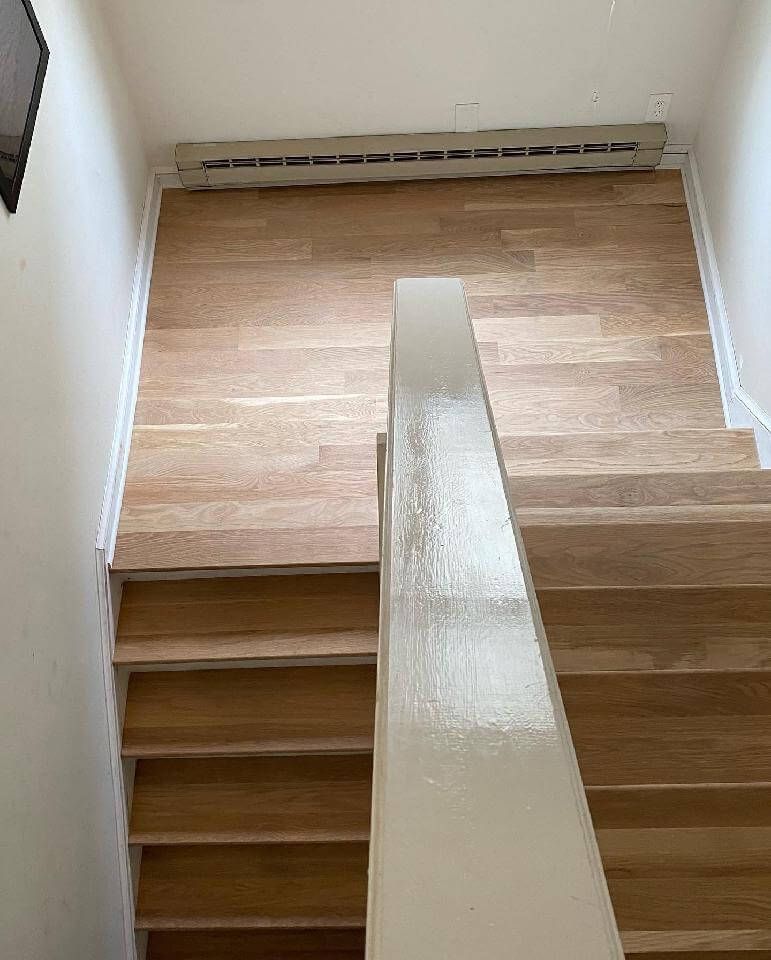 Wooden staircase with a white handrail in a bright hallway, viewed from the bottom landing.