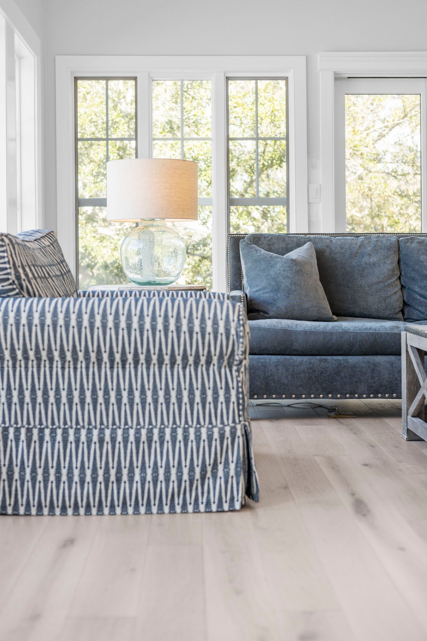 Bright living room with blue patterned armchair, blue sofa, floor lamp, and large windows