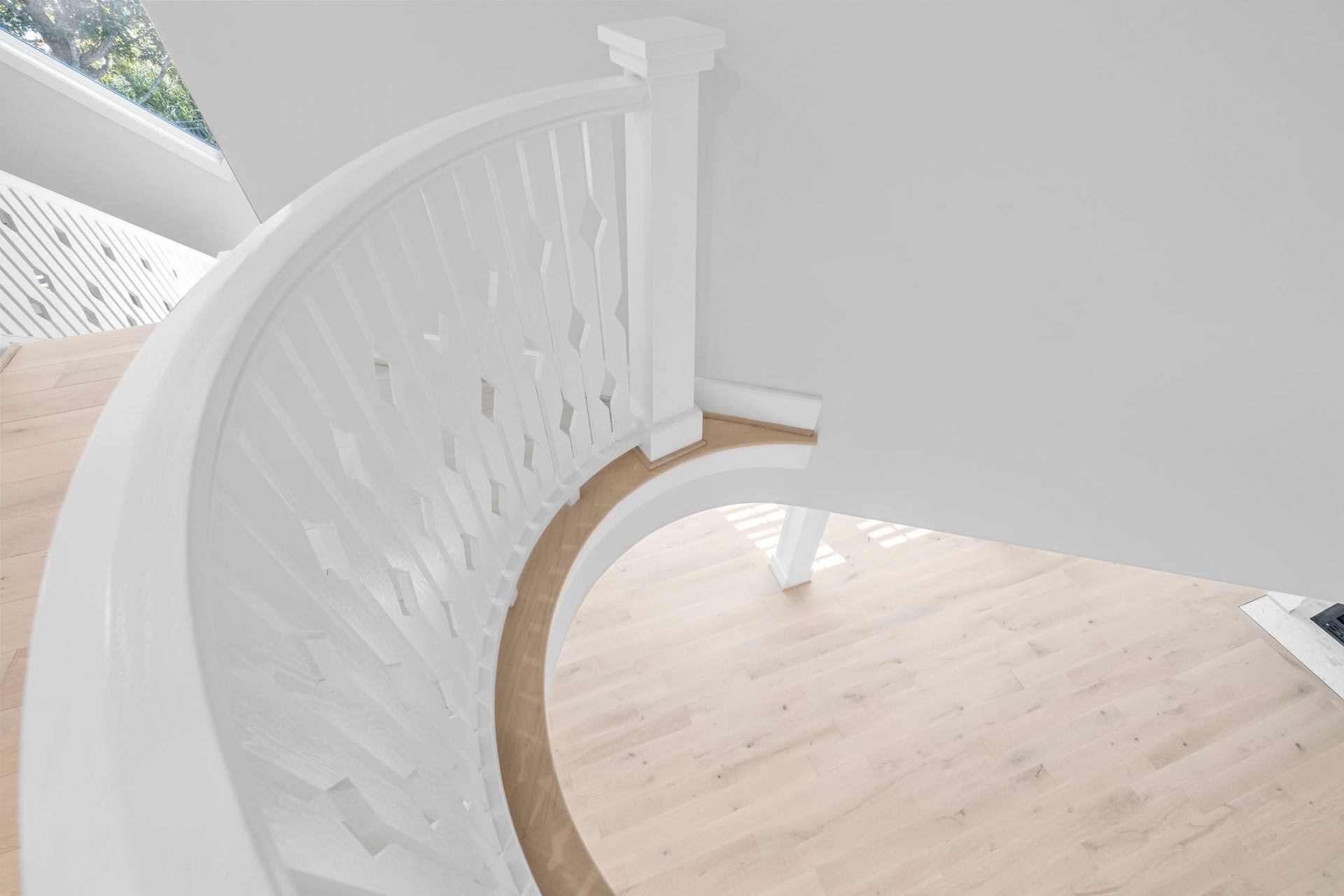 Curved white staircase with decorative railing and light wood floor in a bright interior