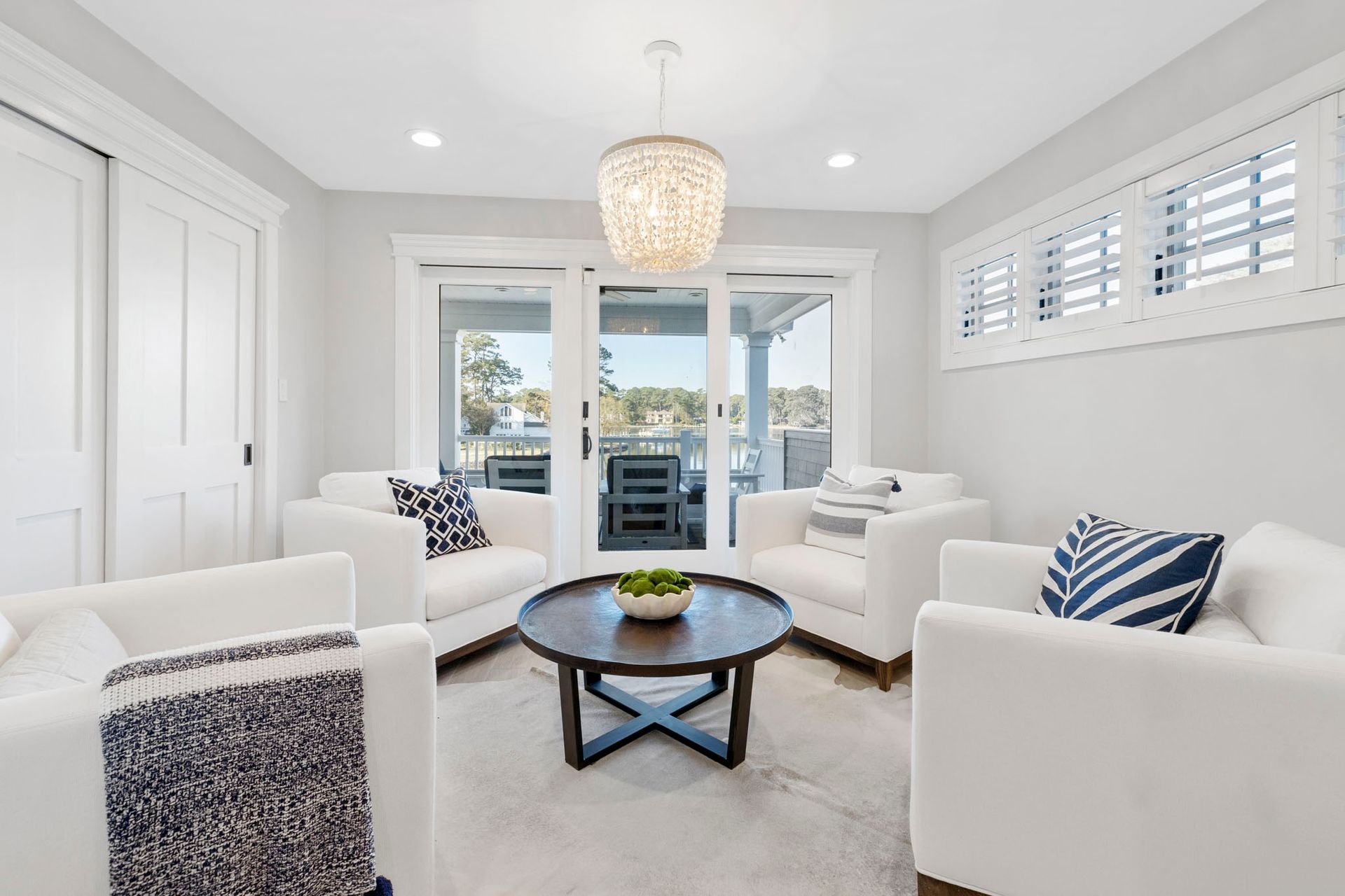 Bright white living room with sofas, armchairs, a round coffee table, and French doors to a patio