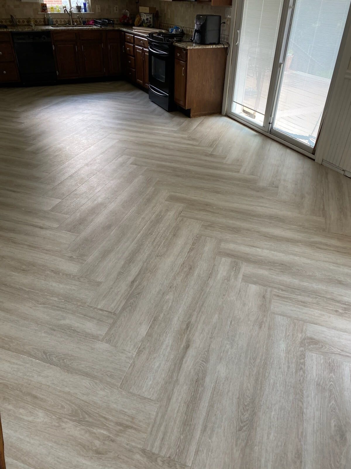 Empty kitchen with light wood herringbone flooring and dark cabinets by sliding glass doors