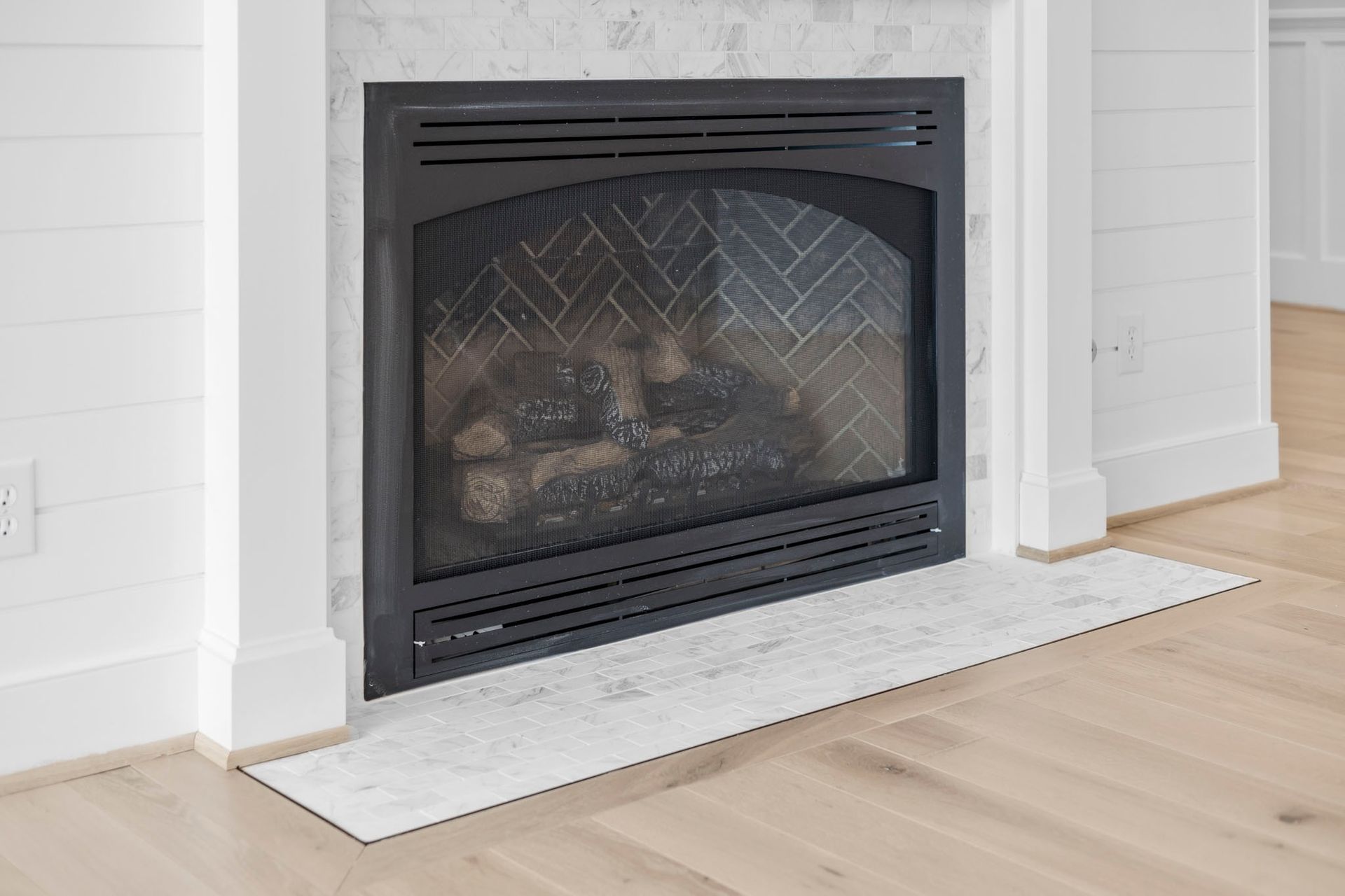 Black fireplace insert in a white wall above a marble hearth on a light wood floor