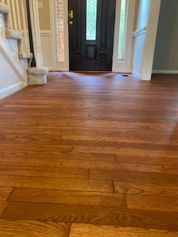 Wooden entryway floor leading to a dark front door in a bright foyer
