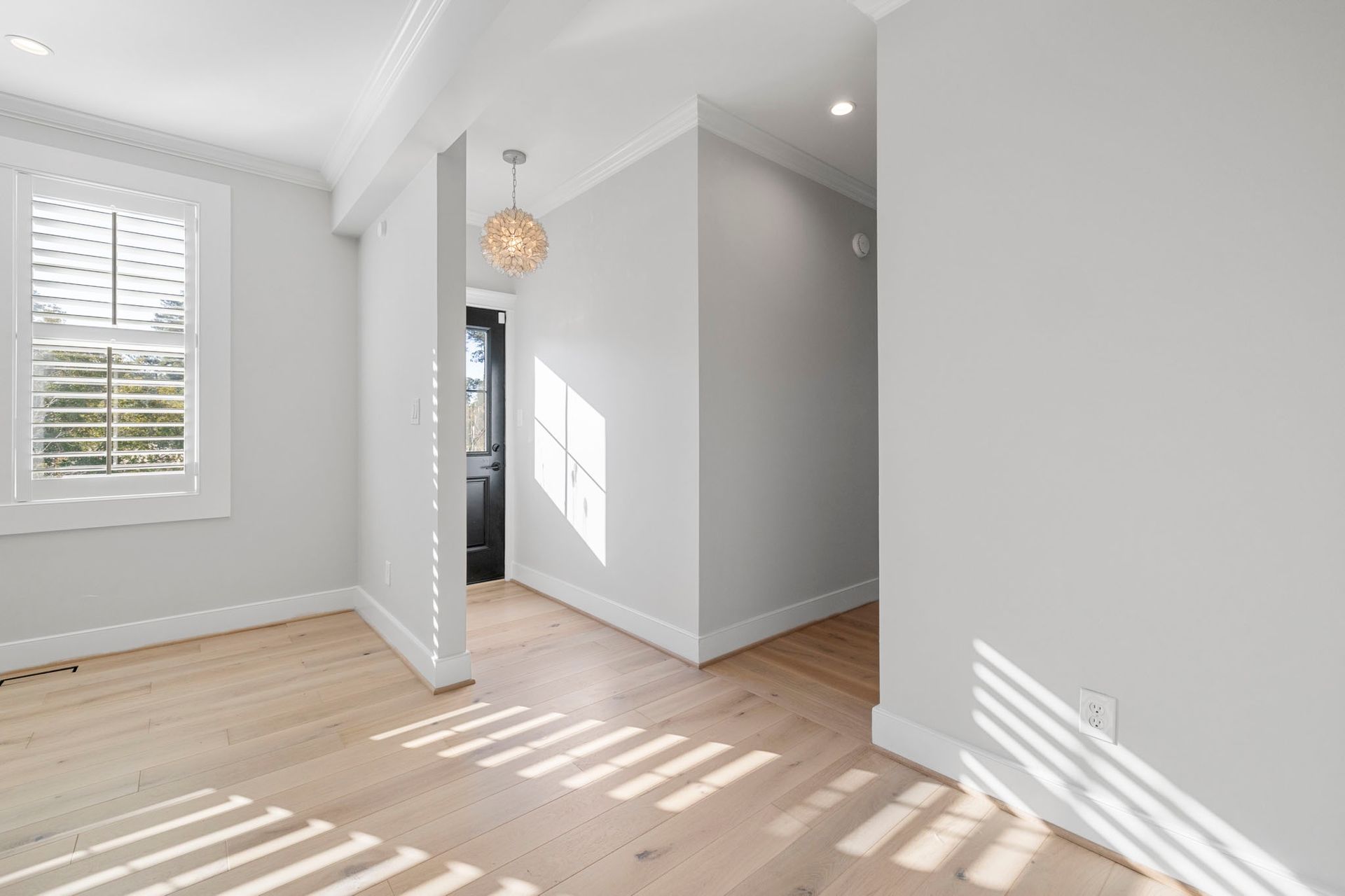 Bright empty room with light wood floors, white walls, and sunlight streaming through a window