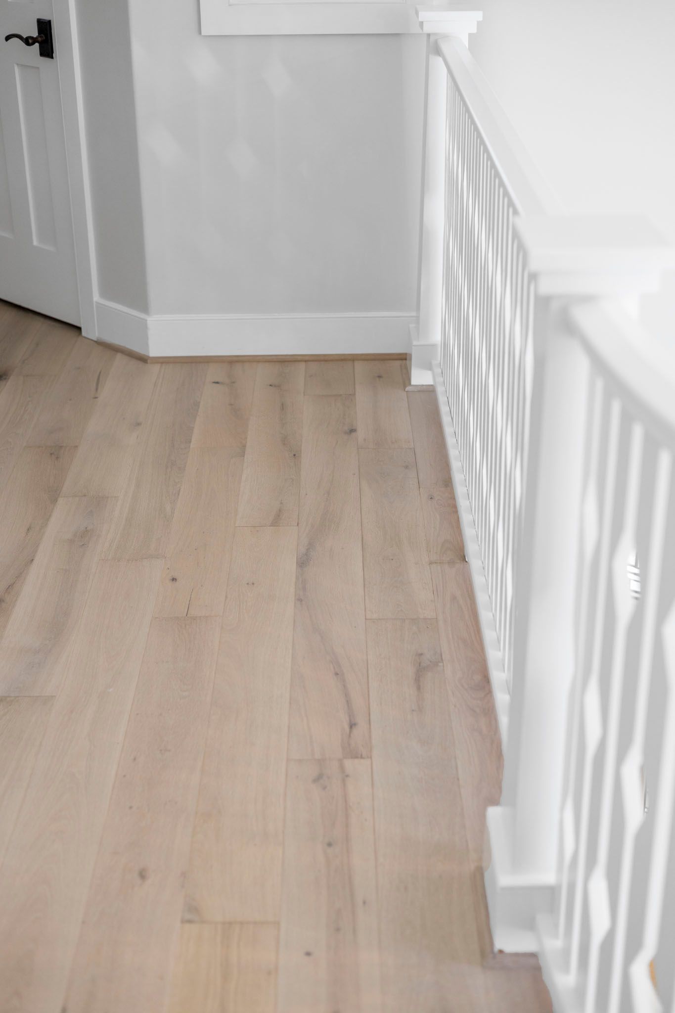 Light wood floor hallway with white walls and railing beside a doorway