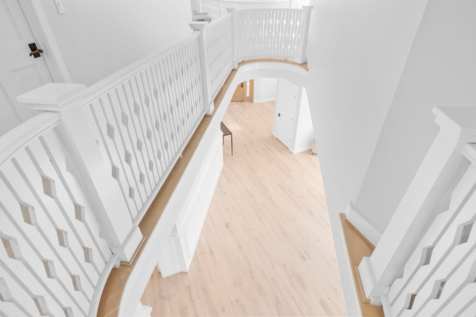 Bright white hallway with light wood floor and white railings on a curved staircase landing