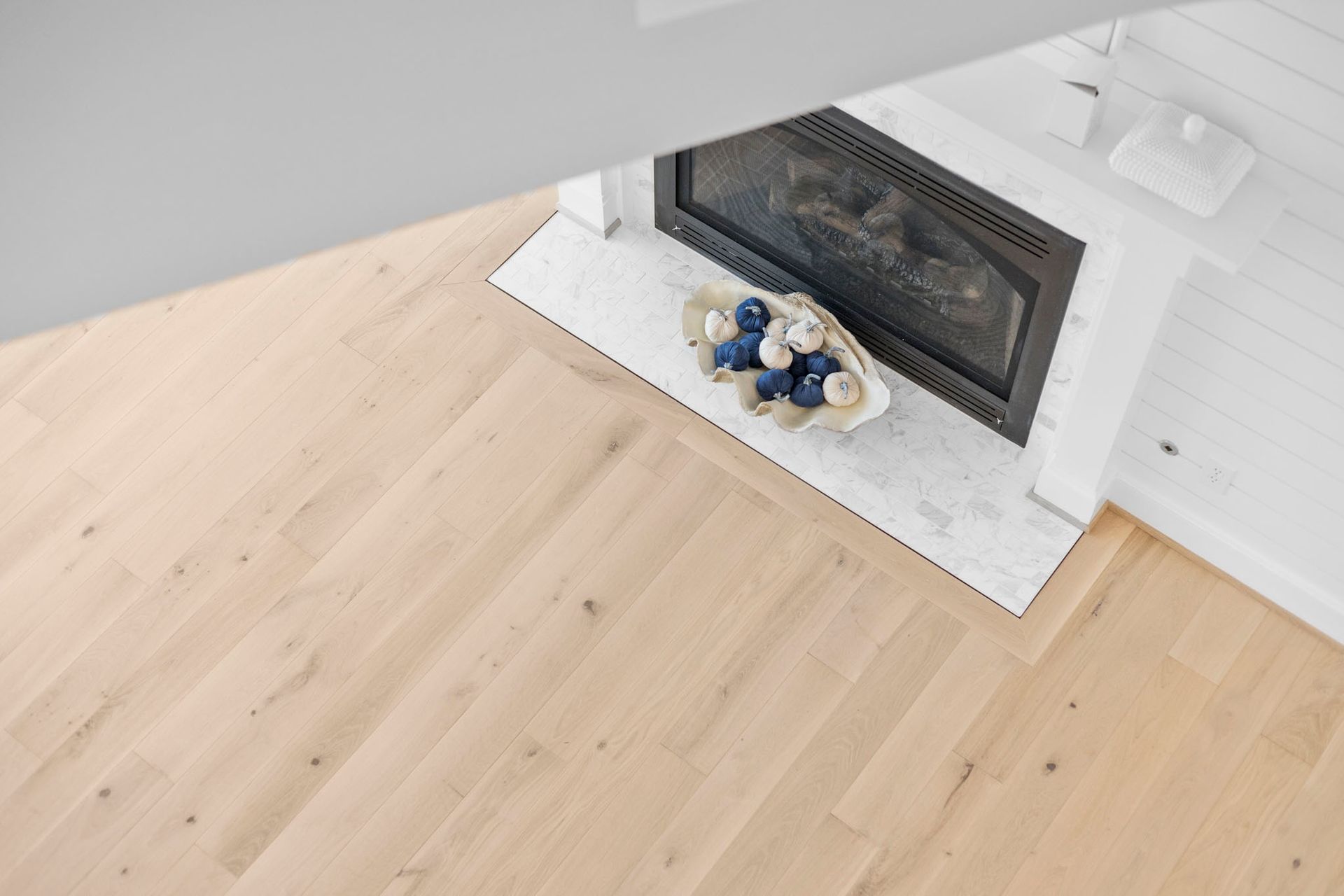Light wood floor beside a white fireplace with a blue-and-white floral tray on the hearth