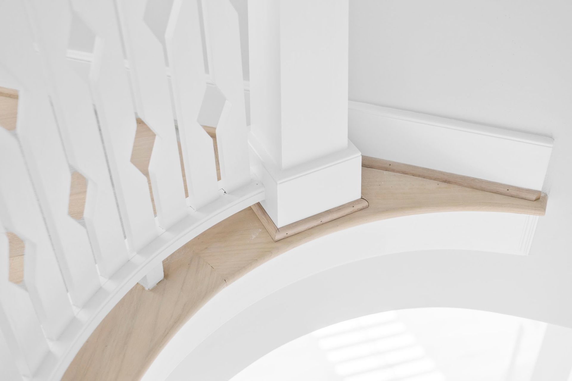 Curved white staircase railing and banister beside a bright interior wall