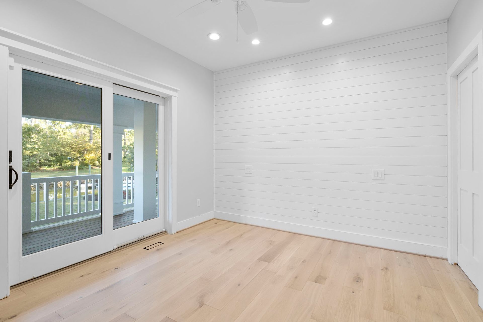 Bright empty room with white walls, light wood floors, and glass doors opening to a balcony.