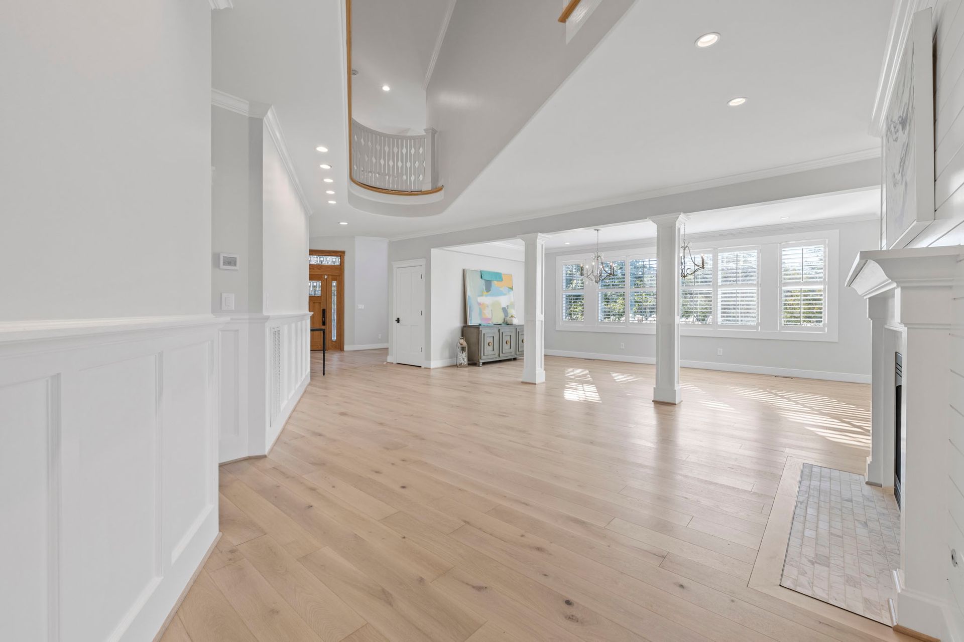 Bright empty living room with light wood floors, white walls, and large windows letting in sunlight