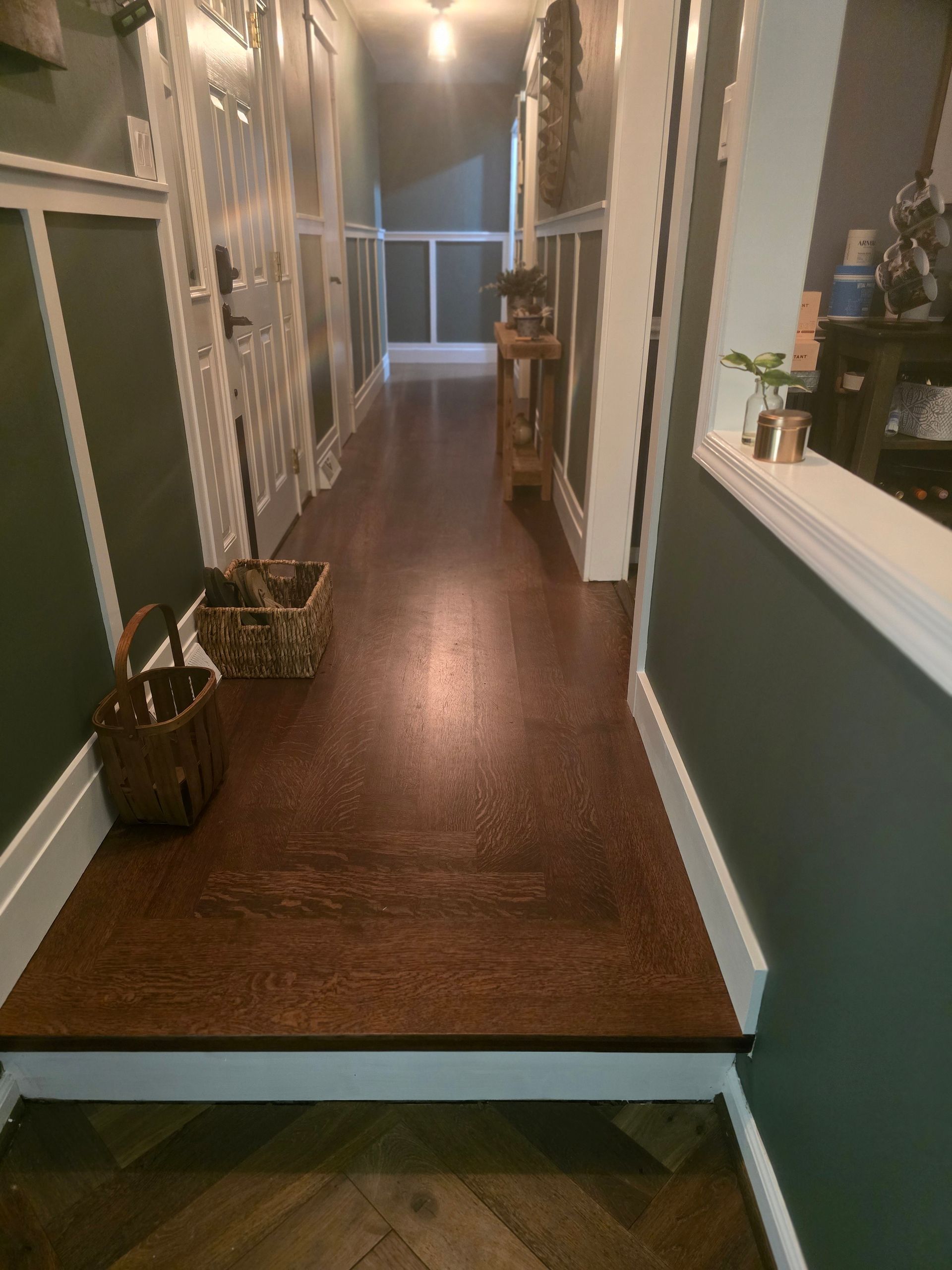 Narrow hallway with dark wood floors, green walls, white trim, and decorative baskets on the left.