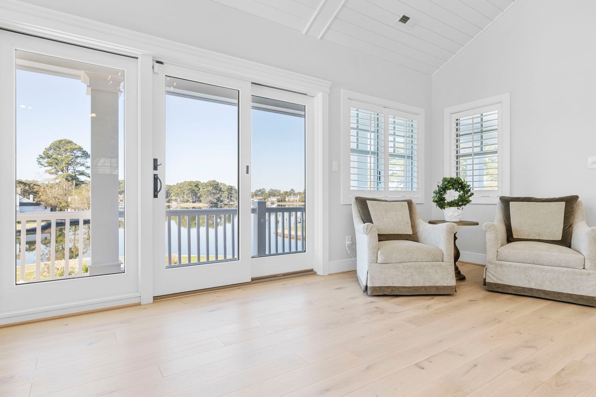 Bright living room with white shutters, sliding glass doors, and two beige chairs by the window.