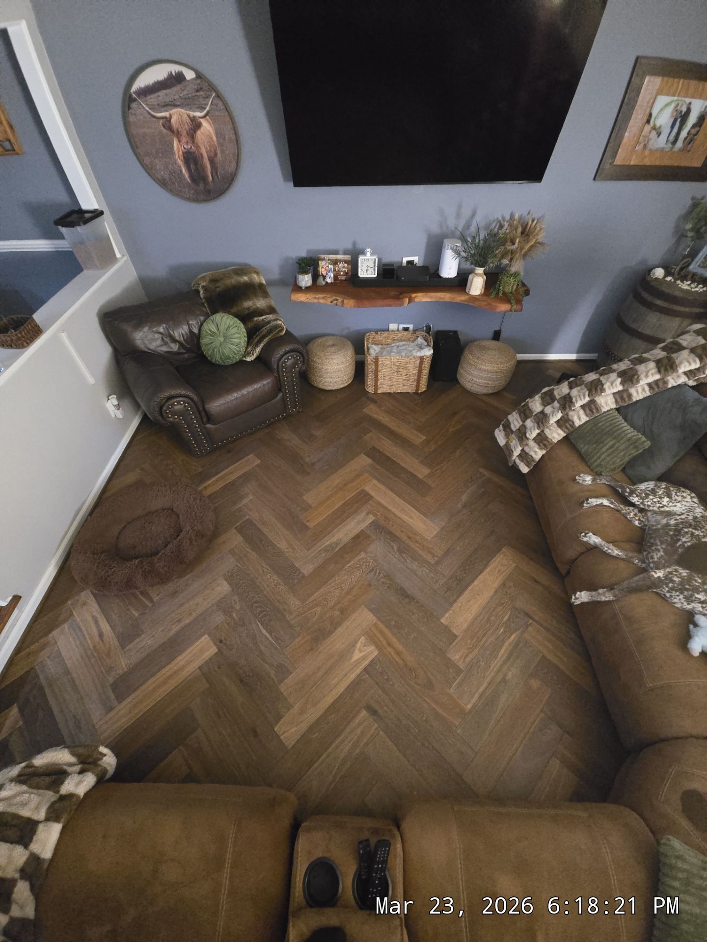 Cozy living room with herringbone wood floor, brown leather sofas, wall TV, and decor on a shelf.