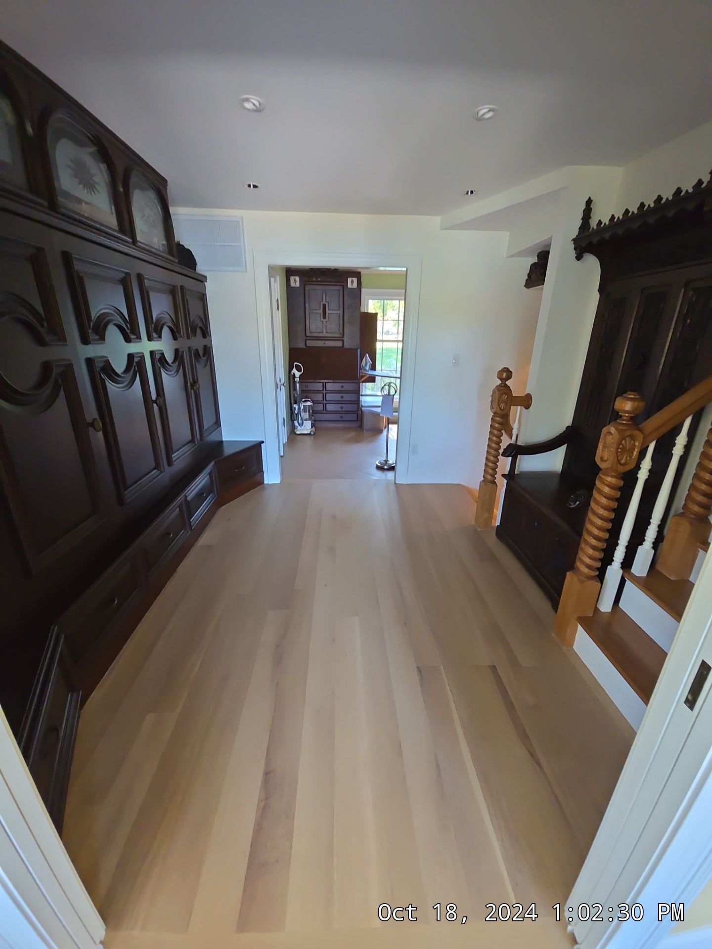 A long hallway with light wood floors, dark wood furniture, and a view into a dining room at the far end