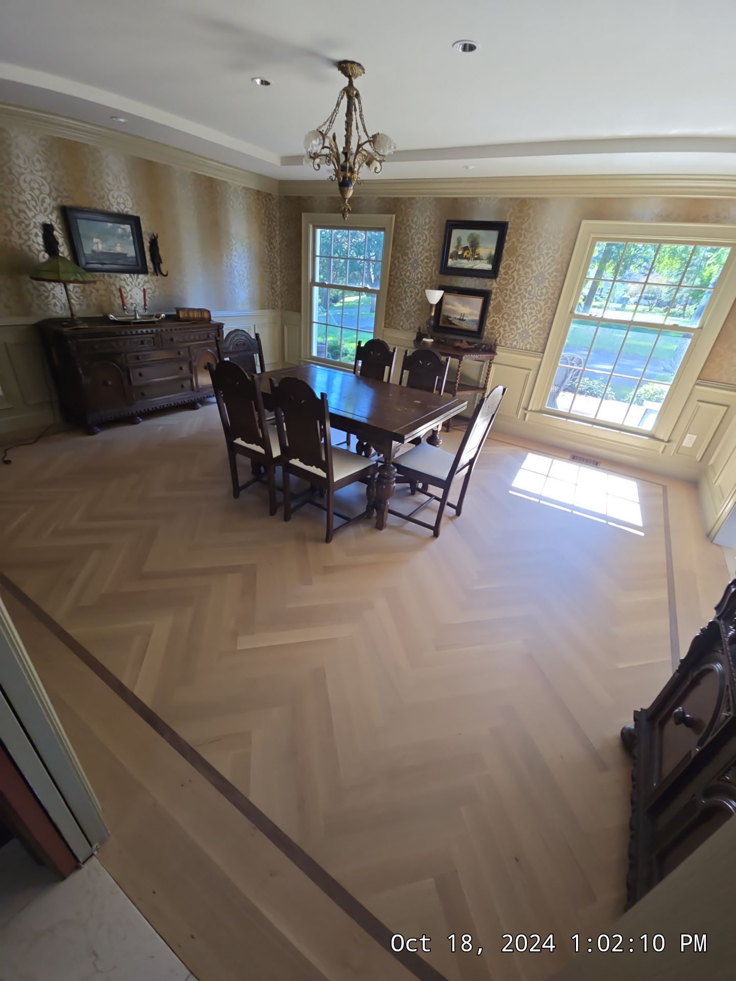Dining room with dark wood table and chairs, chandelier, herringbone floor, and sunlight through bay windows