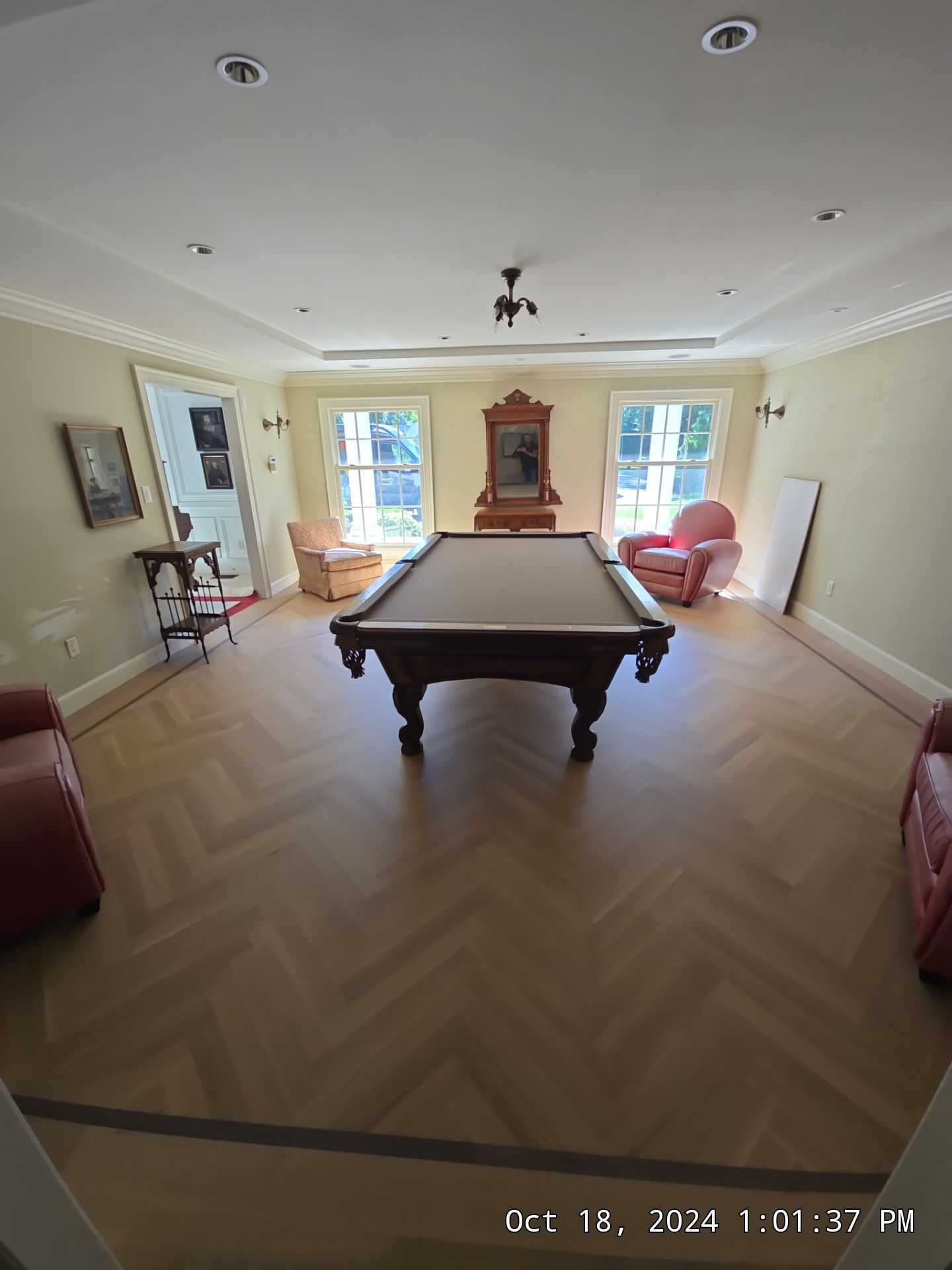 Spacious living room with a pool table centered on herringbone wood floor and chairs by bright windows