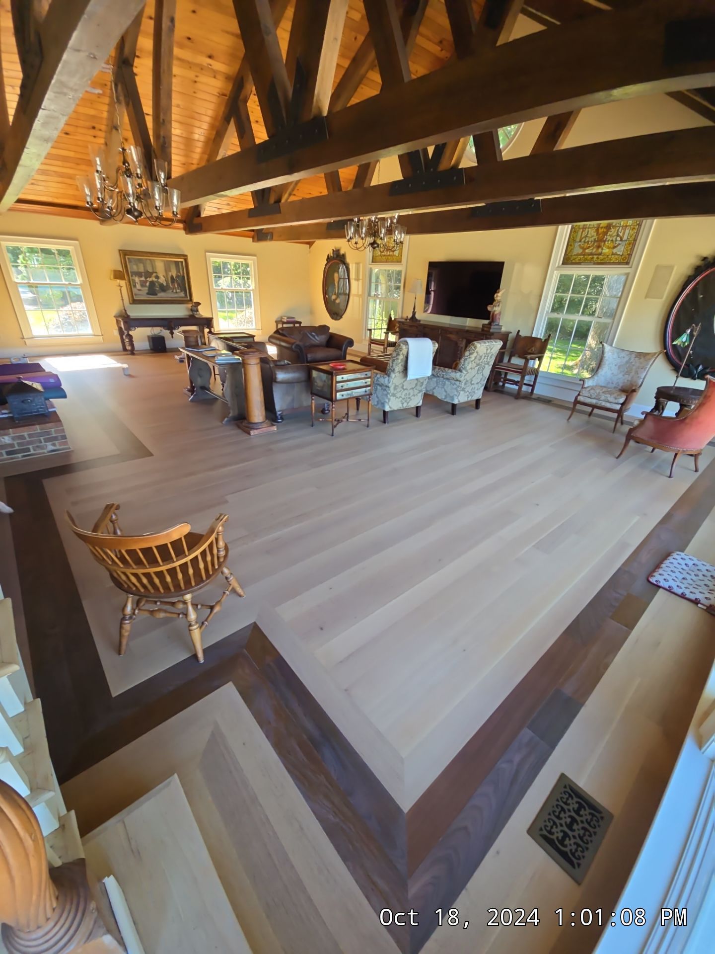 Wide rustic living room with exposed beams, fireplace, sofas, chairs, and large windows