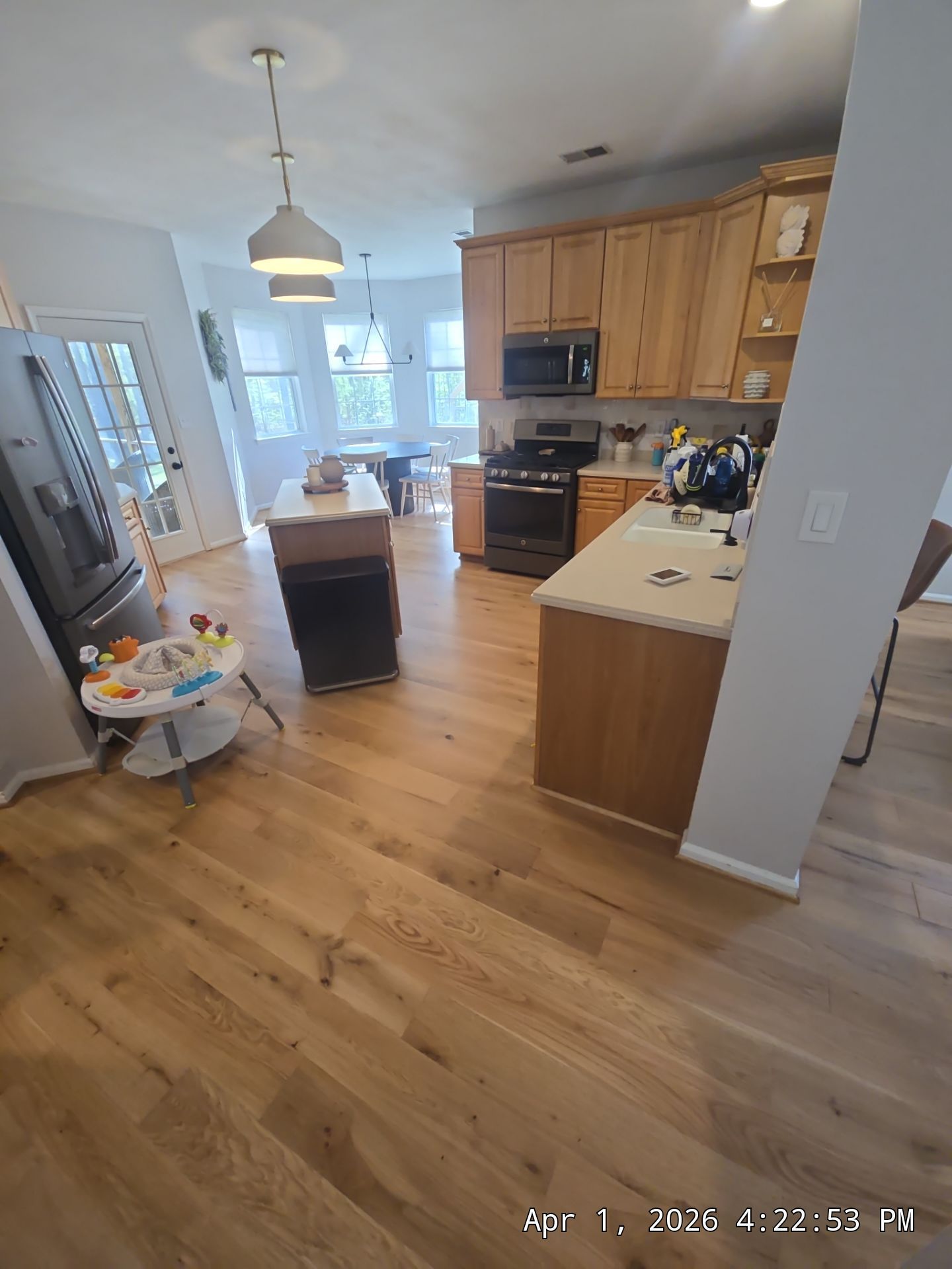 Bright kitchen with wood floors, oak cabinets, black appliances, and a child’s activity seat in the foreground.