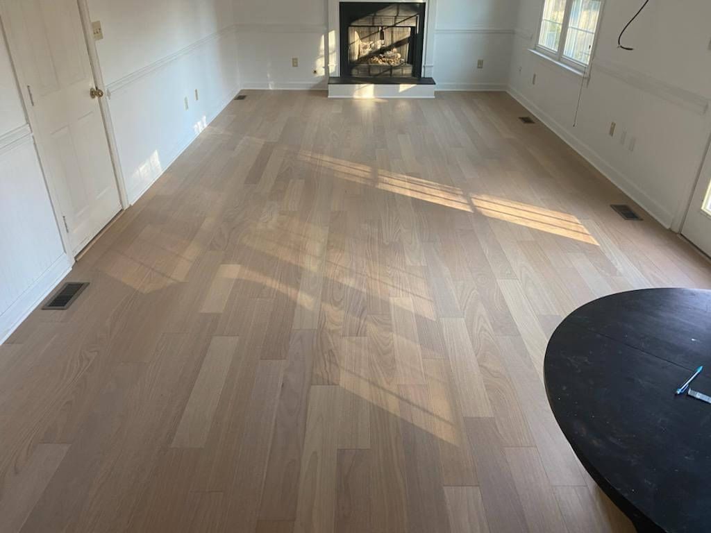 Empty living room with light wood floors, white walls, fireplace, and sunlight streaming through windows