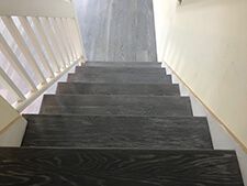 Dark wooden staircase with white railings and walls, viewed from the top looking downward