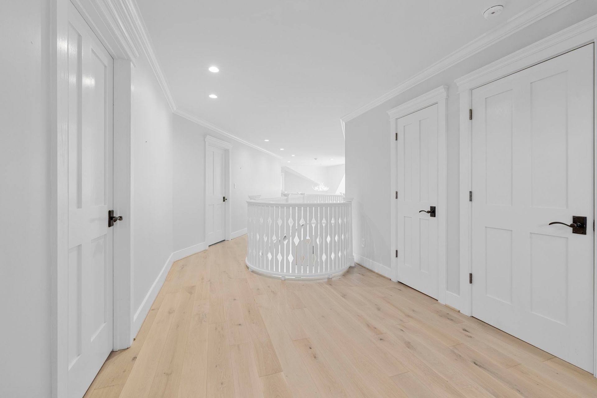 Bright white hallway with light wood floors, multiple doors, and a curved railing near the end.
