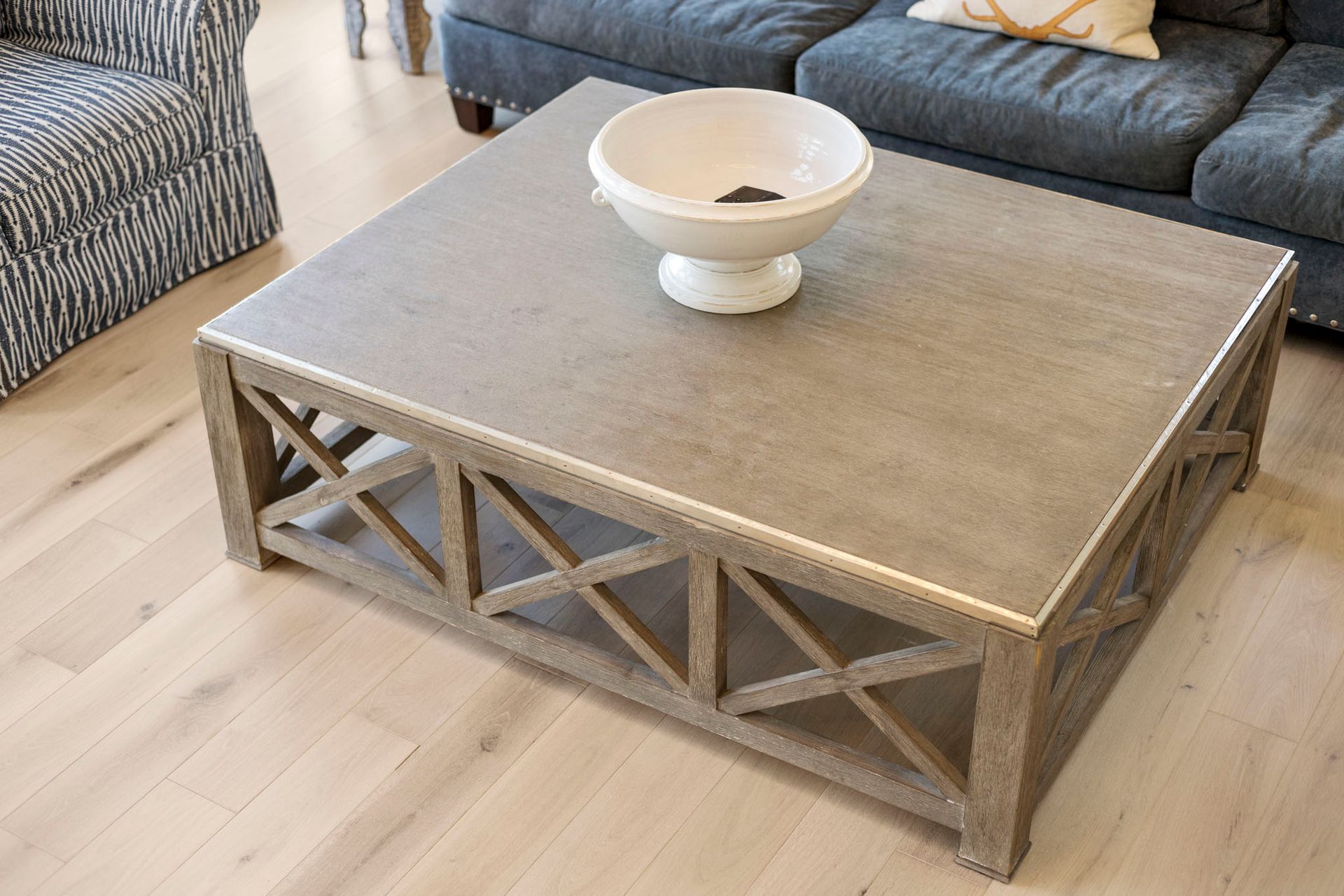Gray wood coffee table in a living room, with a white bowl on top and sofas in the background