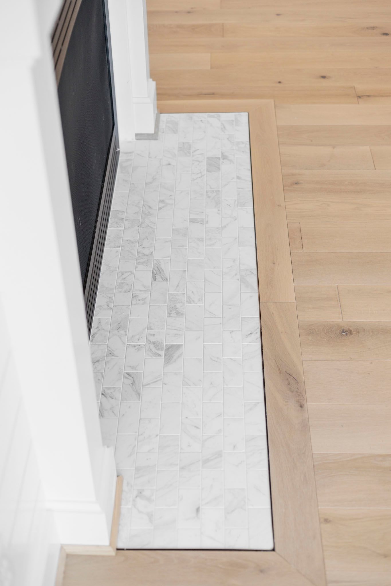 Narrow white runner rug beside a black baby gate on a light wood floor in a hallway
