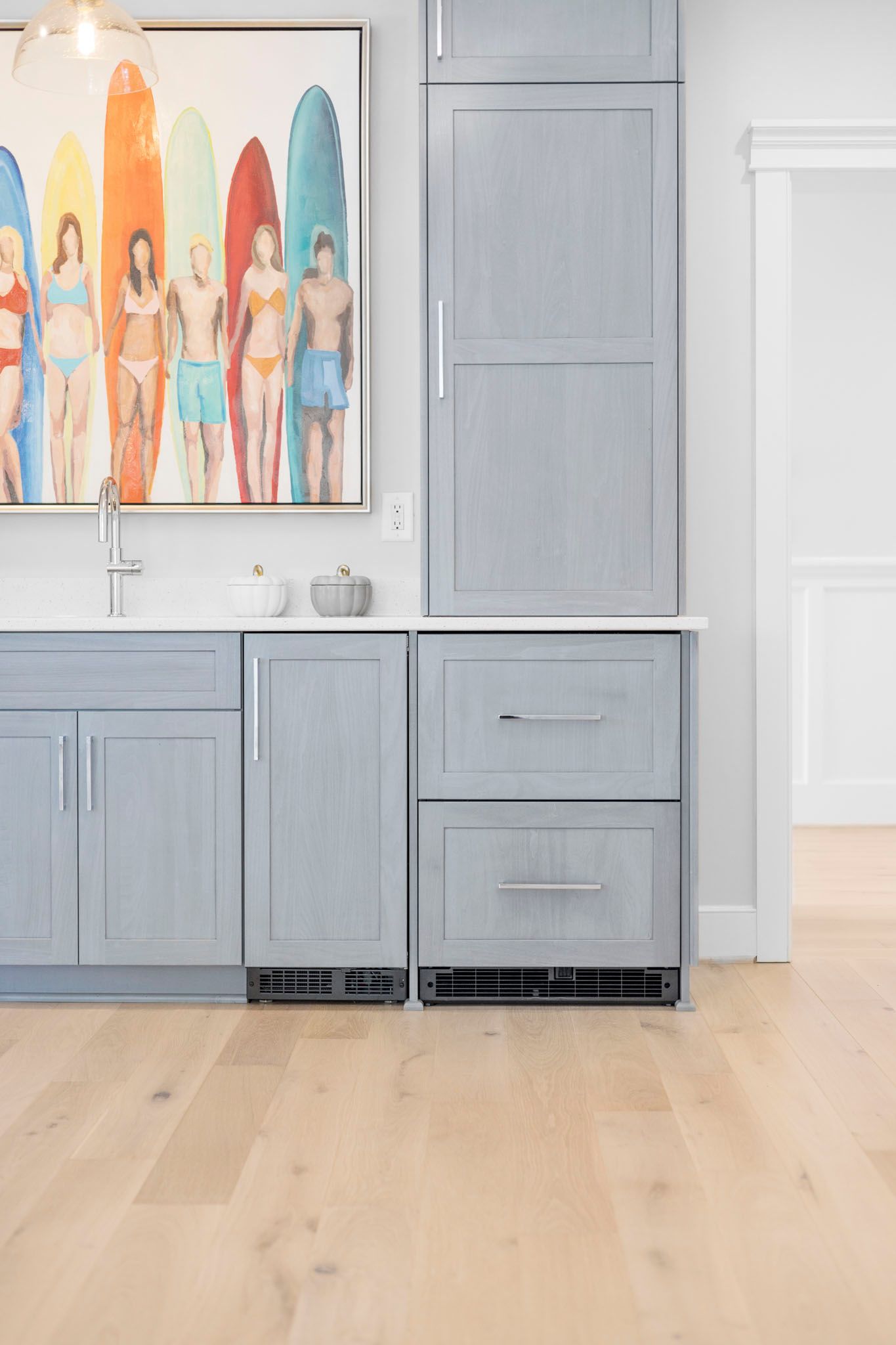Bright kitchen with light blue cabinets, white countertops, and a colorful wall painting above the sink.