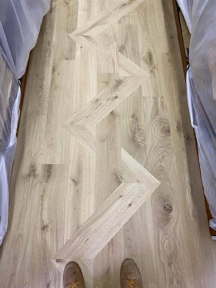 Wooden herringbone-pattern flooring between fabric-covered sides, viewed from above with shoes at the bottom.