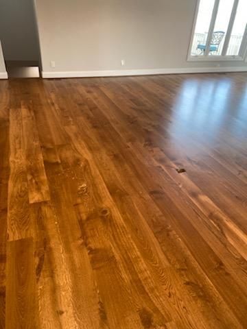 Empty room with glossy medium-brown hardwood floors and a window letting in daylight