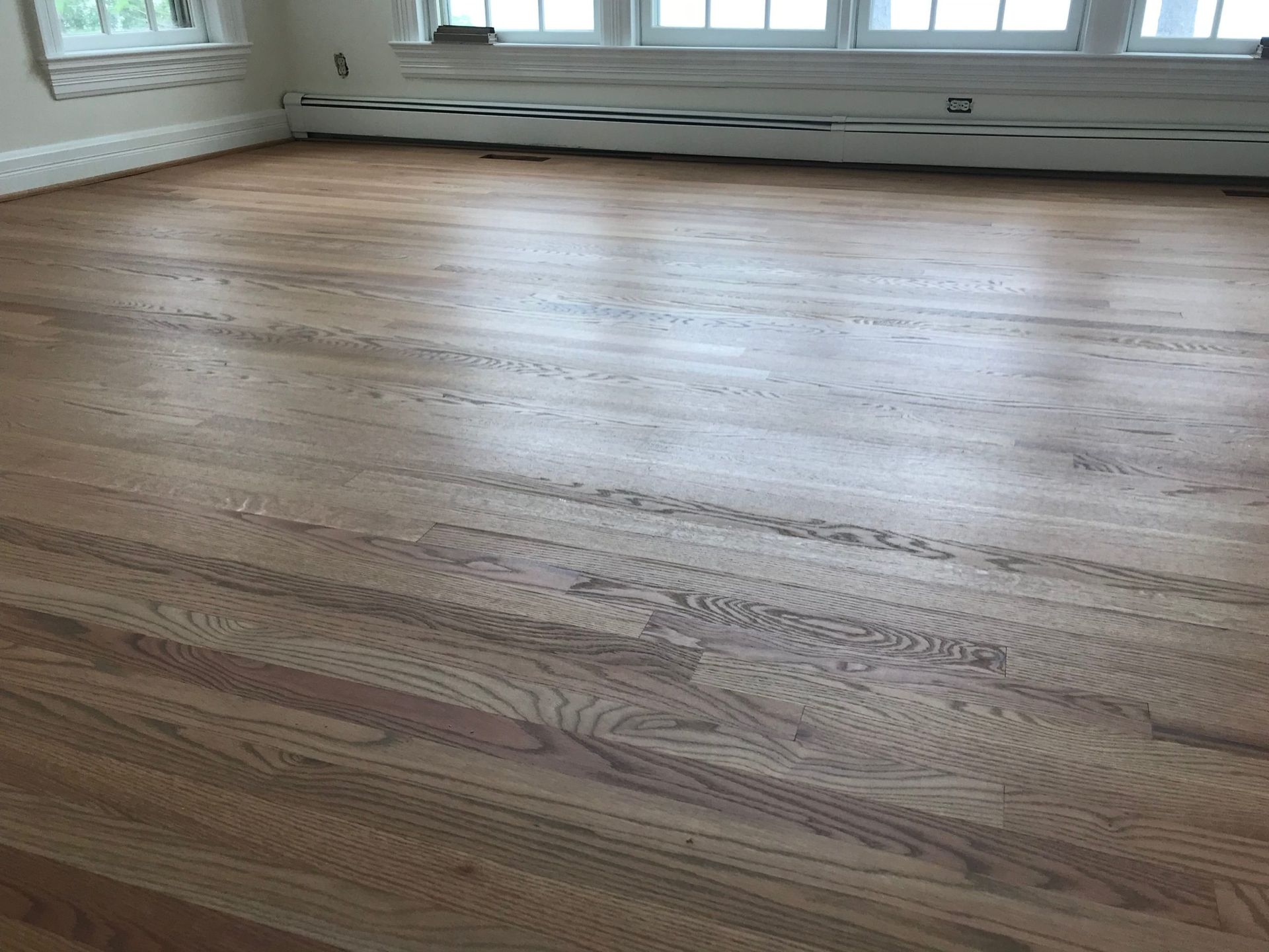 Empty hardwood floor in a bright room with large windows and white walls