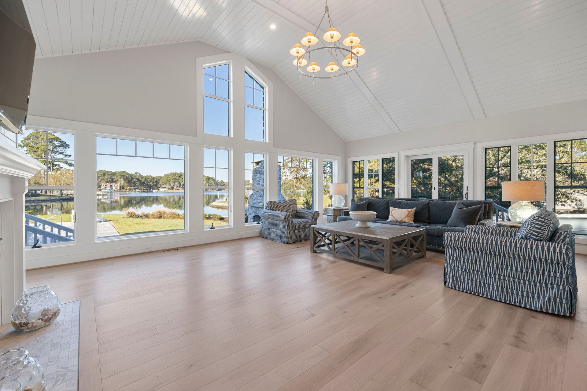 Bright living room with large windows, light wood floors, blue sofas, and a chandelier.