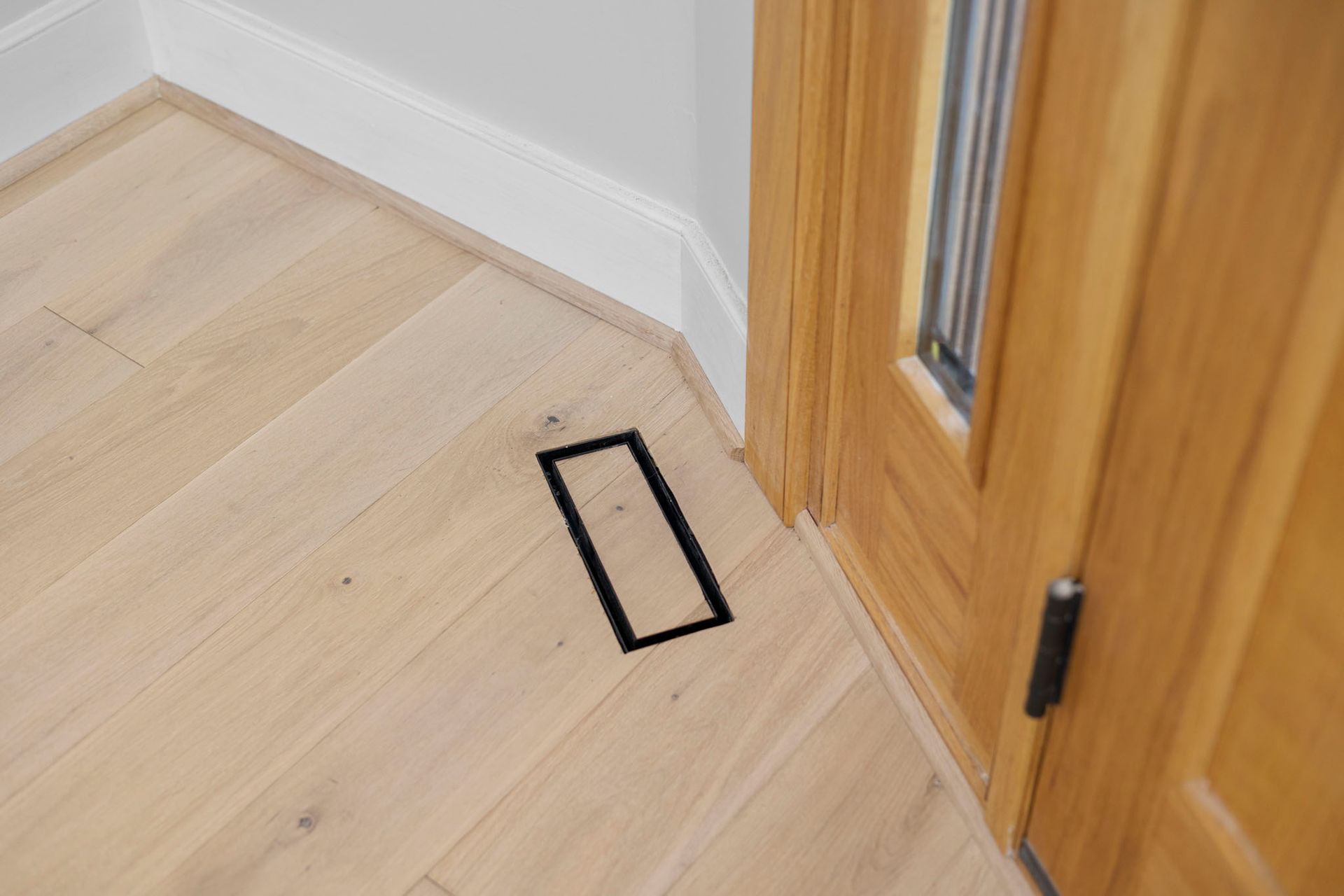 Black rectangular floor marking beside a wooden door on a light wood floor