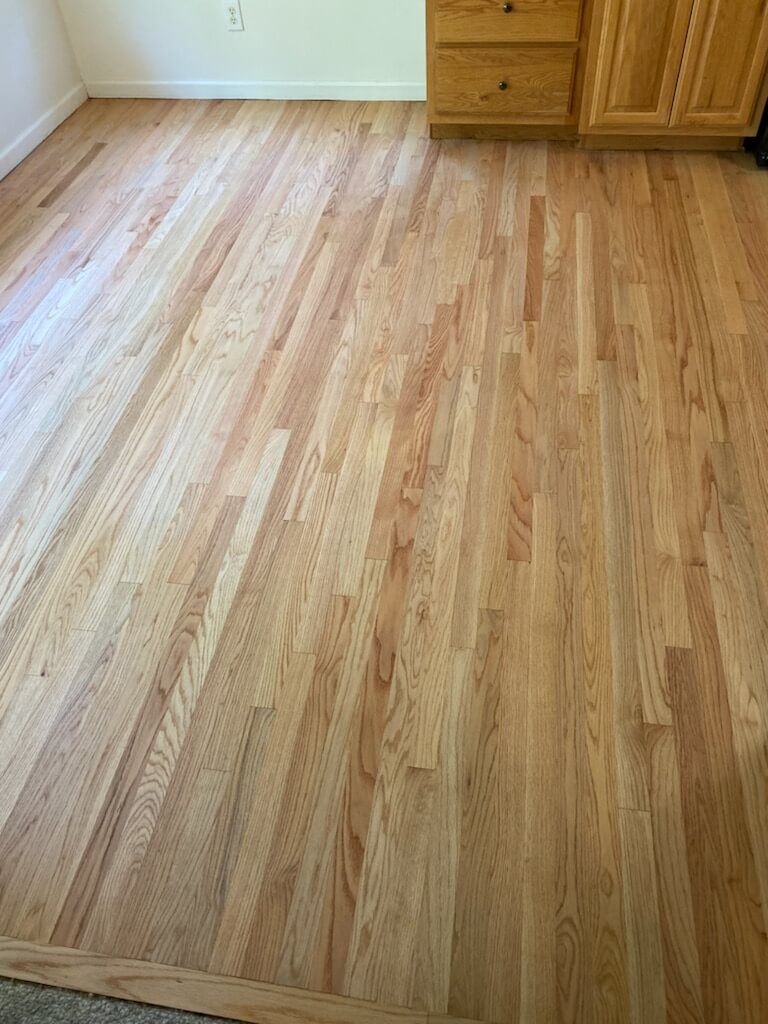 Light wood flooring in an empty room beside a wooden dresser and cabinet.