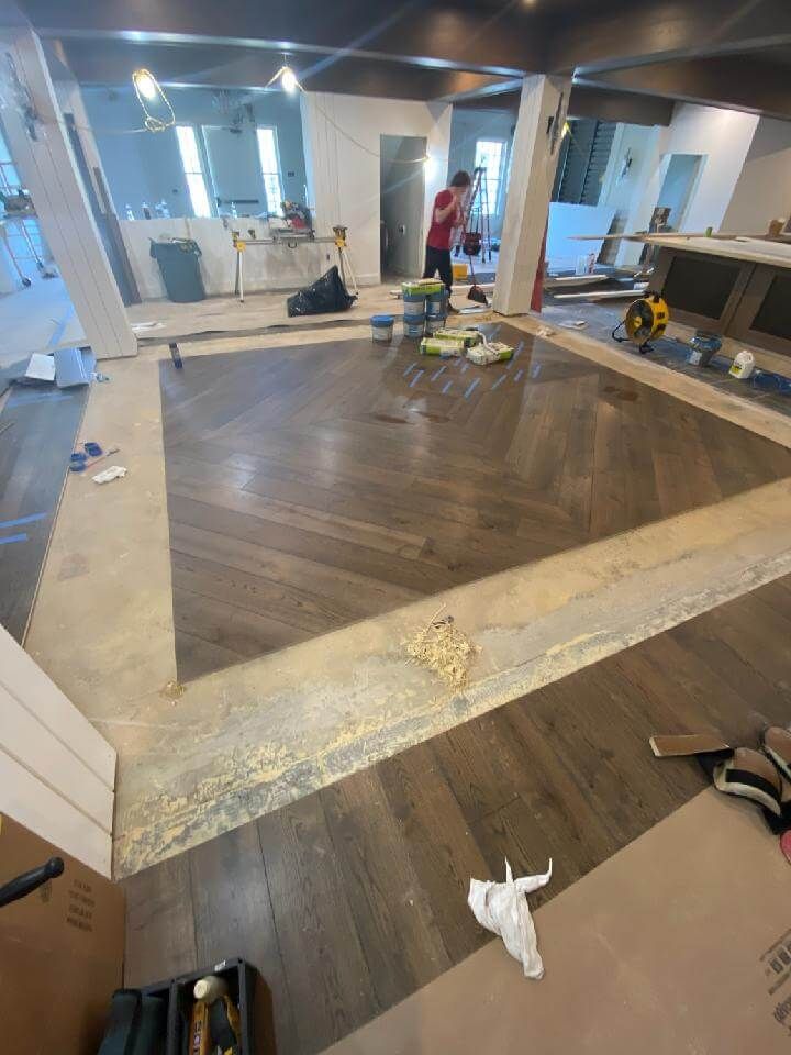 Partially renovated room with a large recessed wooden floor area, tools, and workers in the background