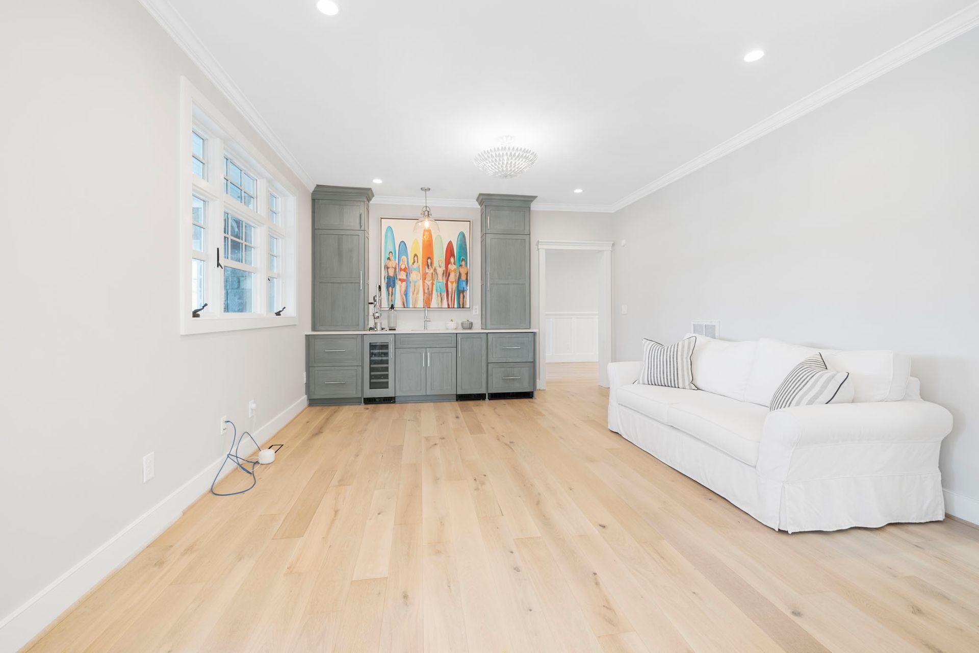 Bright modern living room with light wood floors, white sofa, and gray built-in cabinets with artwork.