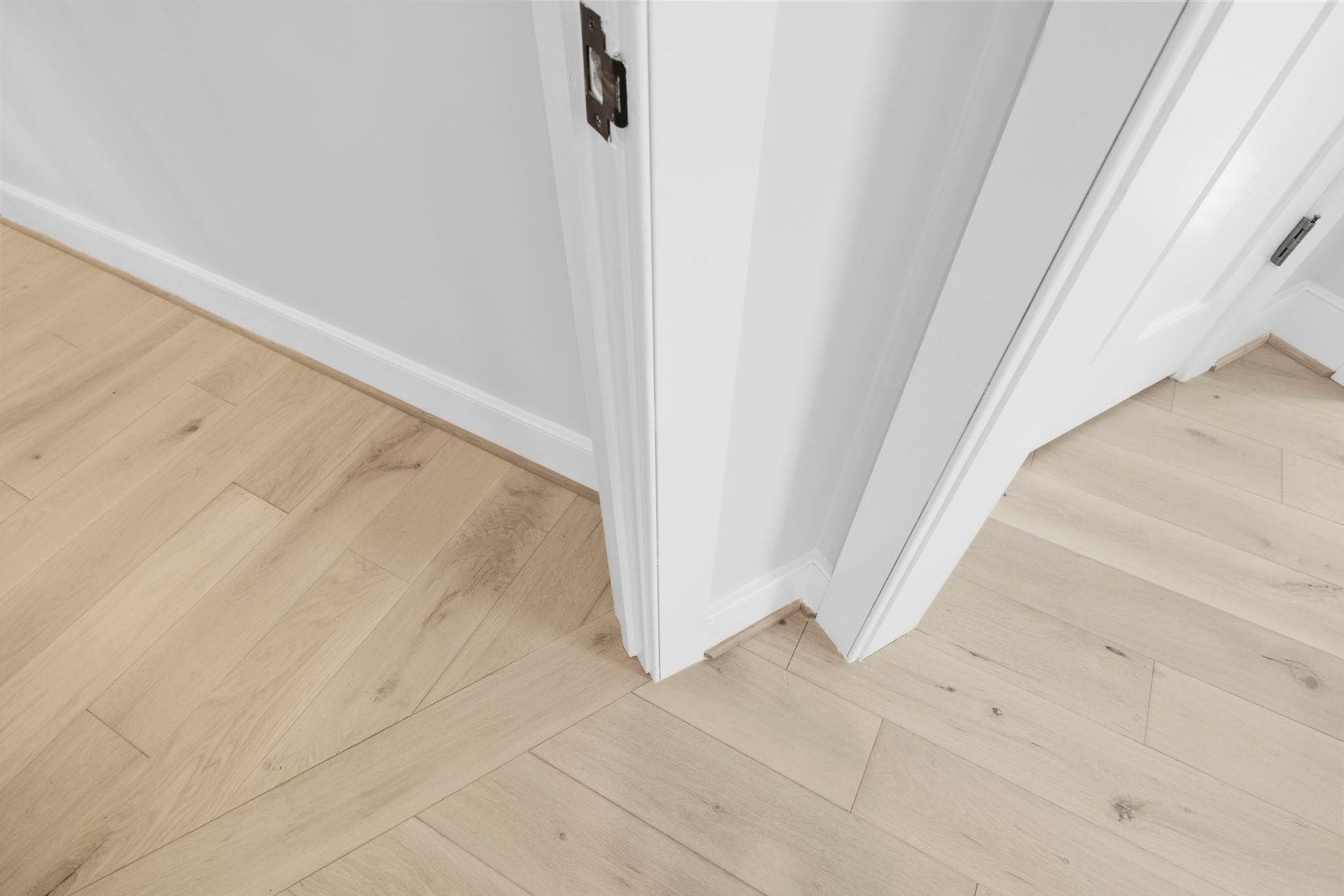 Light wood flooring meeting white walls and door frames at a hallway corner.