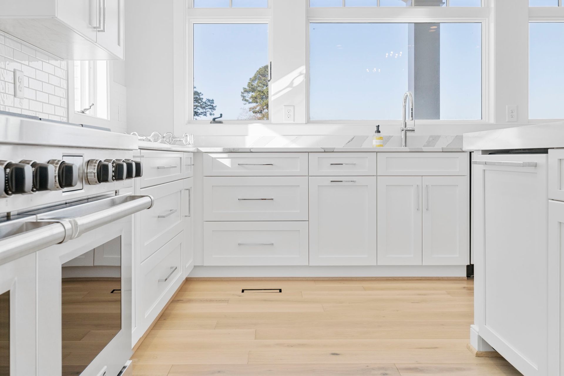Bright white kitchen with a gas stove, marble countertops, and large windows over light wood floors