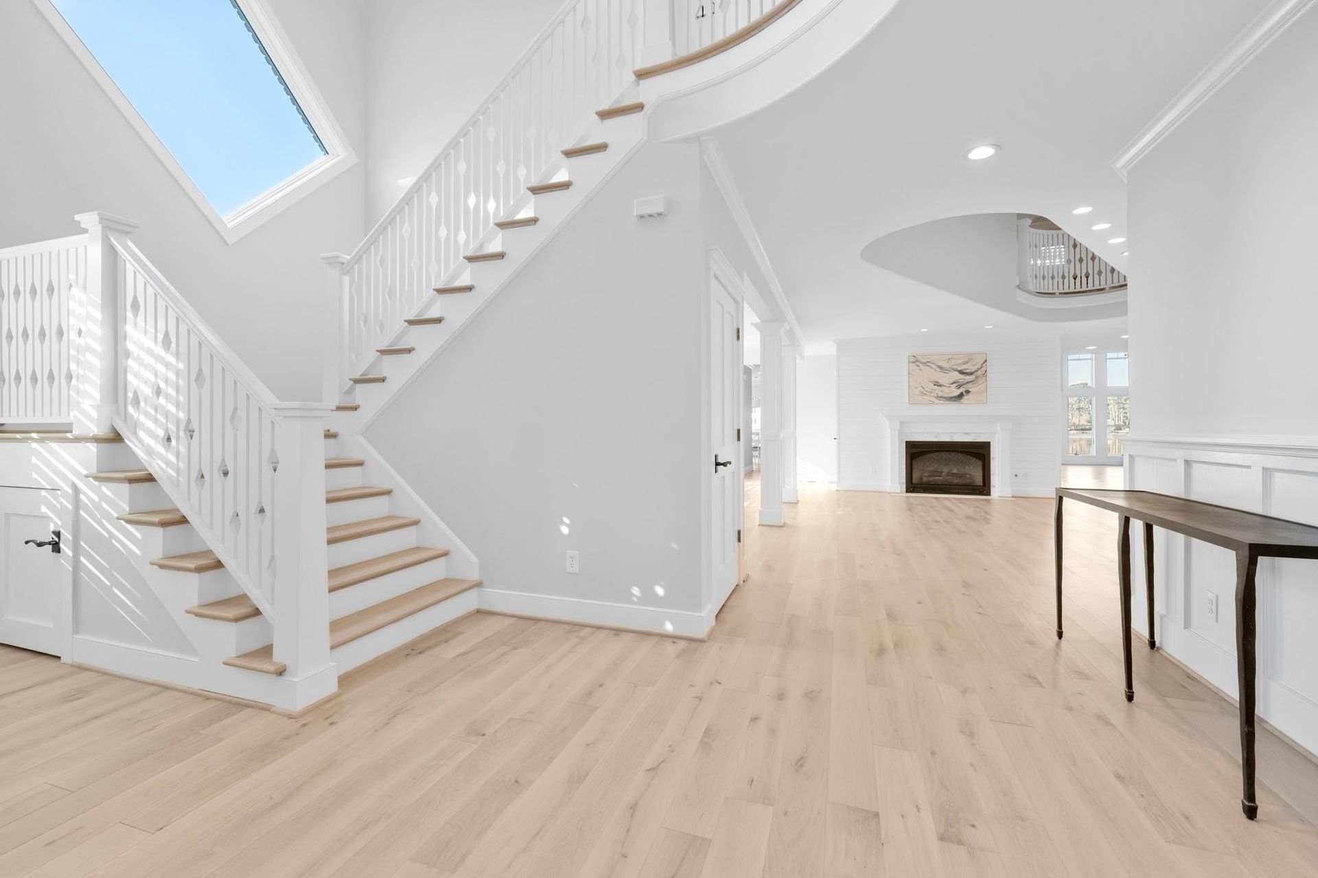 Bright modern foyer with white staircase, light wood floors, and a fireplace in the distance